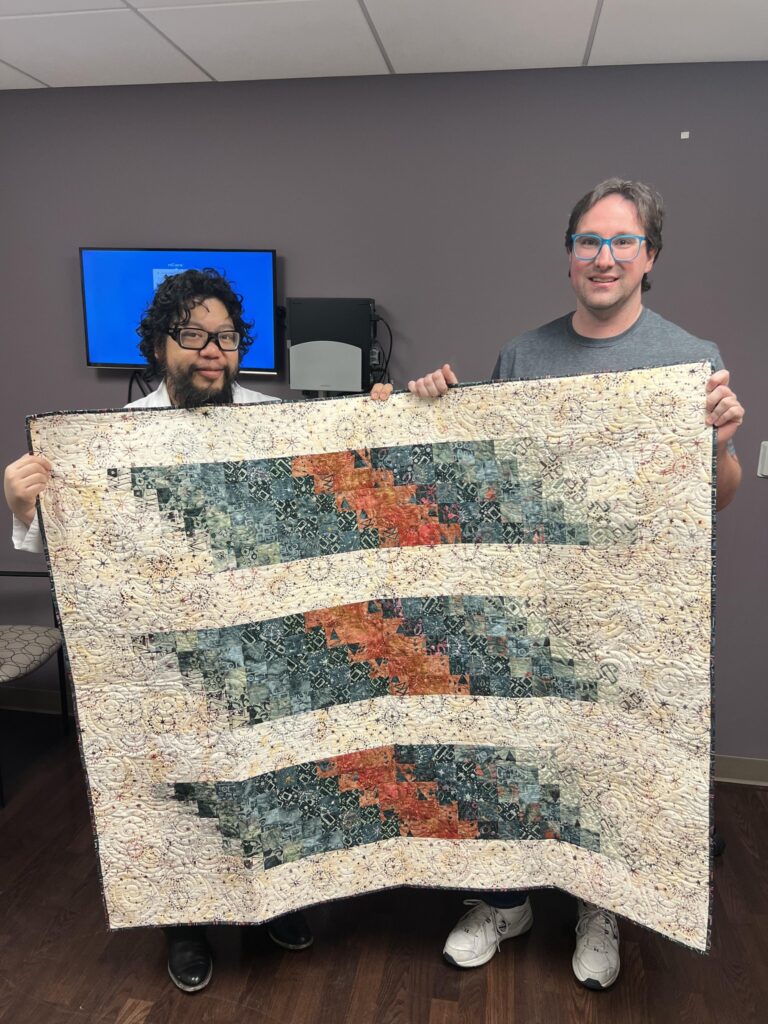 Two men holding up a quilt